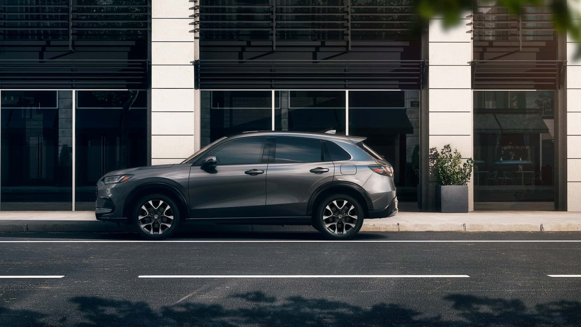 A gray Honda HR-V in profile, parked on a street curb outside a building