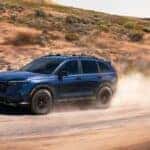 A blue Honda CR-V kicking up dust as it drives on a dirt road in a desert