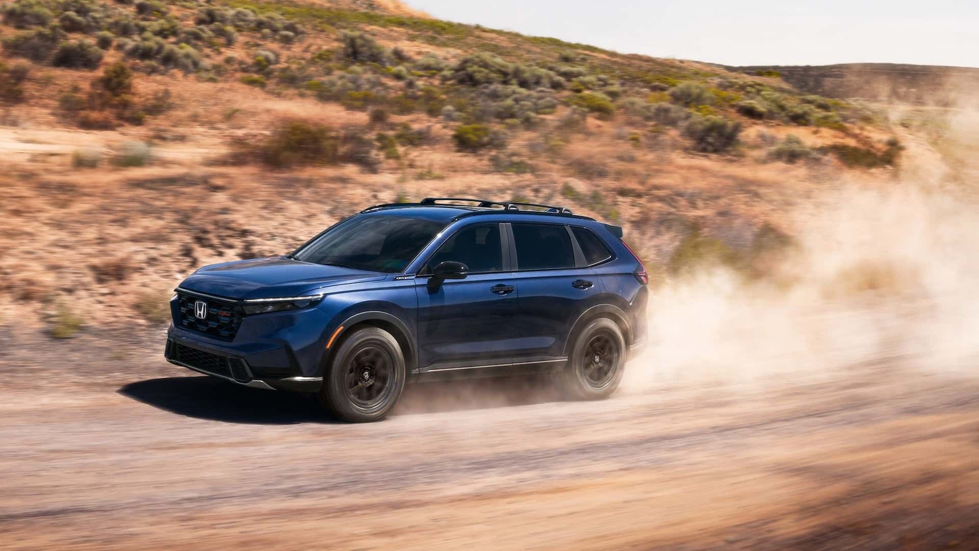 A blue Honda CR-V kicking up dust as it drives on a dirt road in a desert