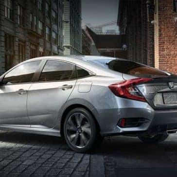 Woman standing on the sidewalk near a silver 2019 Honda Civic Sport