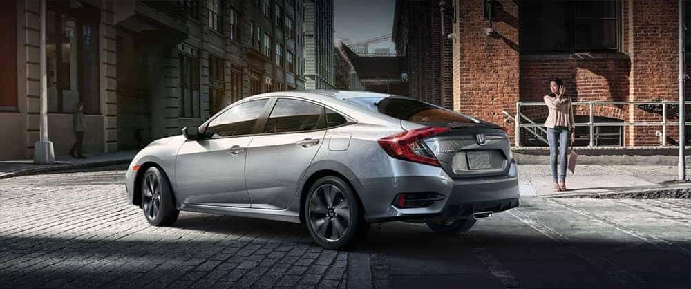 Woman standing on the sidewalk near a silver 2019 Honda Civic Sport