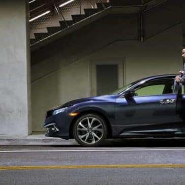 Man getting into the driver's seat of a blue 2020 Honda Civic parked on the side of the road