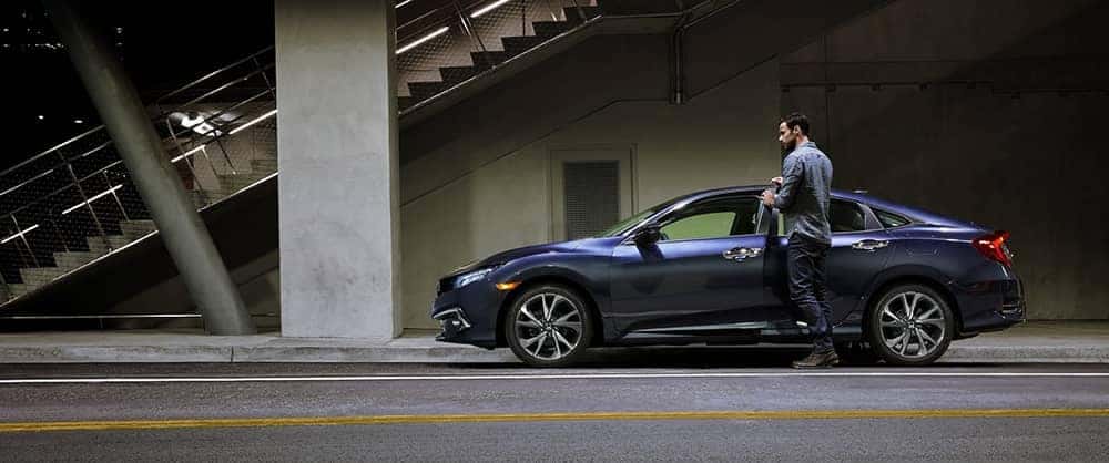 Man getting into the driver's seat of a blue 2020 Honda Civic parked on the side of the road