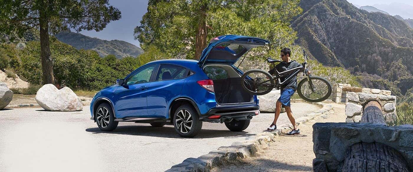 Man putting a bike in the trunk of his blue Honda HR-V in the mountains