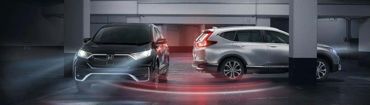 A silver Honda CR-V backing up toward a black CR-V in a parking garage