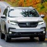 A white 2022 Honda Pilot Black Edition is shown driving on an empty road after visiting a Honda dealer near you.