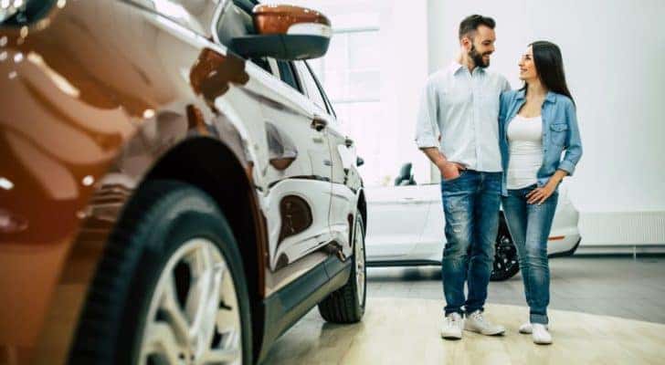 A couple is shown standing in a dealership after asking how to 'sell my car.'