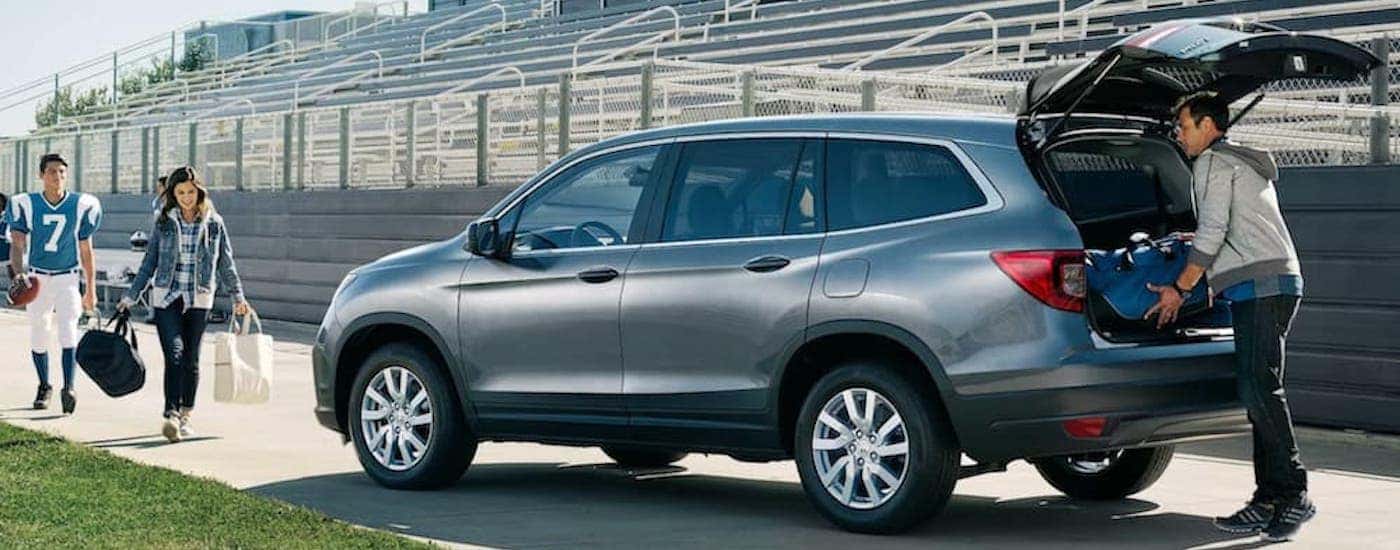 A grey 2021 Honda Pilot is shown from the rear at an angle while being loaded with sports equipment.