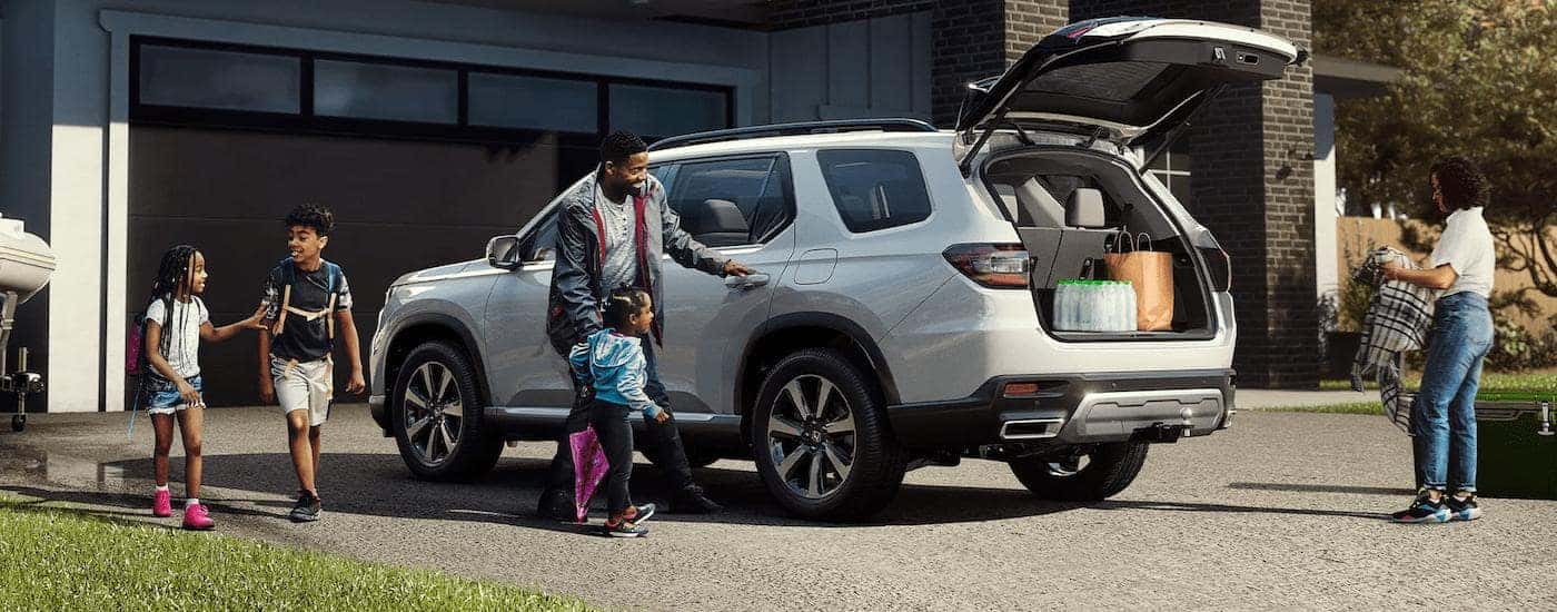 A white 2023 Honda Pilot is shown from a rear angle as a family loads it with luggage.