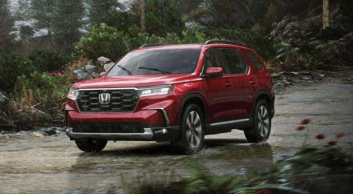 A red 2023 Honda Pilot Elite for sale is shown driving on a rainy day.