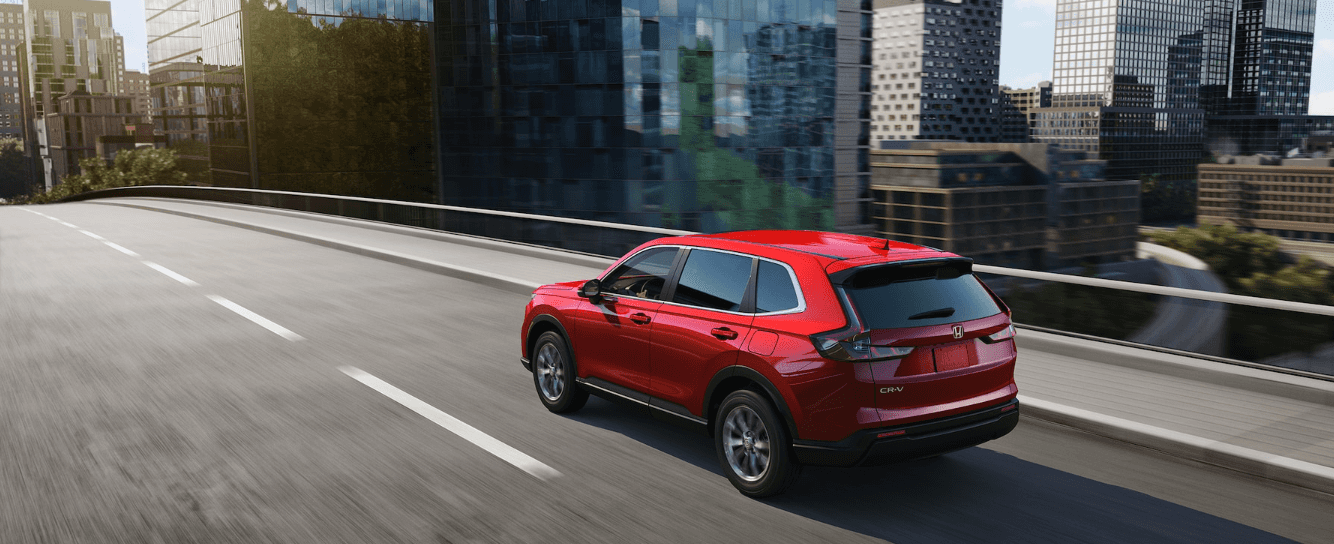 The 2025 Honda CR-V EX in Radiant Red Metallic driving over a city bridge