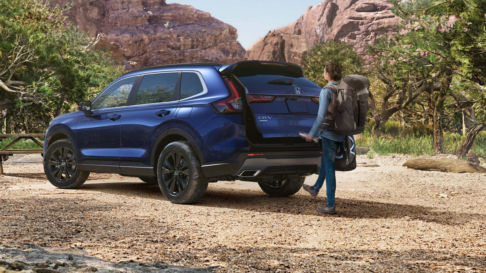 Someone opening the trunk of a blue Honda CR-V on a dirt road in a desert
