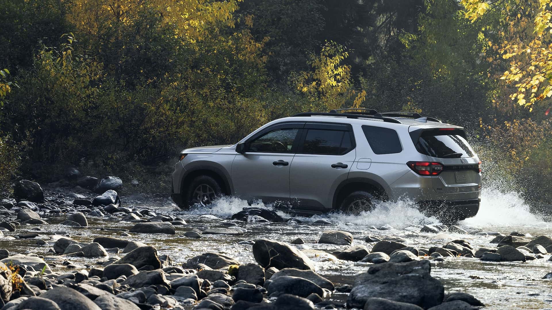 A gray 2025 Honda Pilot driving throw a brook in a forest