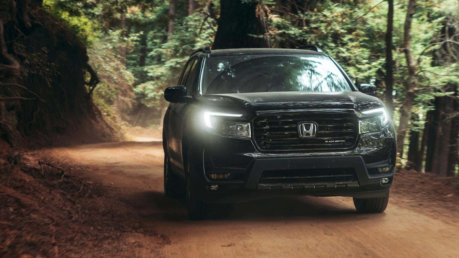 A black Honda Passport driving over a dirt road through a forest