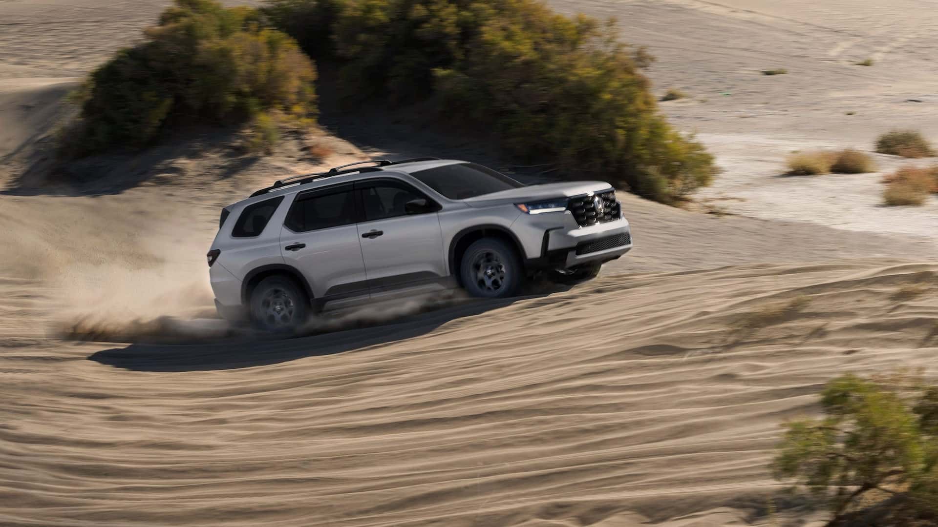 A silver Honda Pilot driving up a sand dune in the desert
