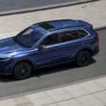 A blue Honda CR-V driving quickly down the road by a pair of joggers