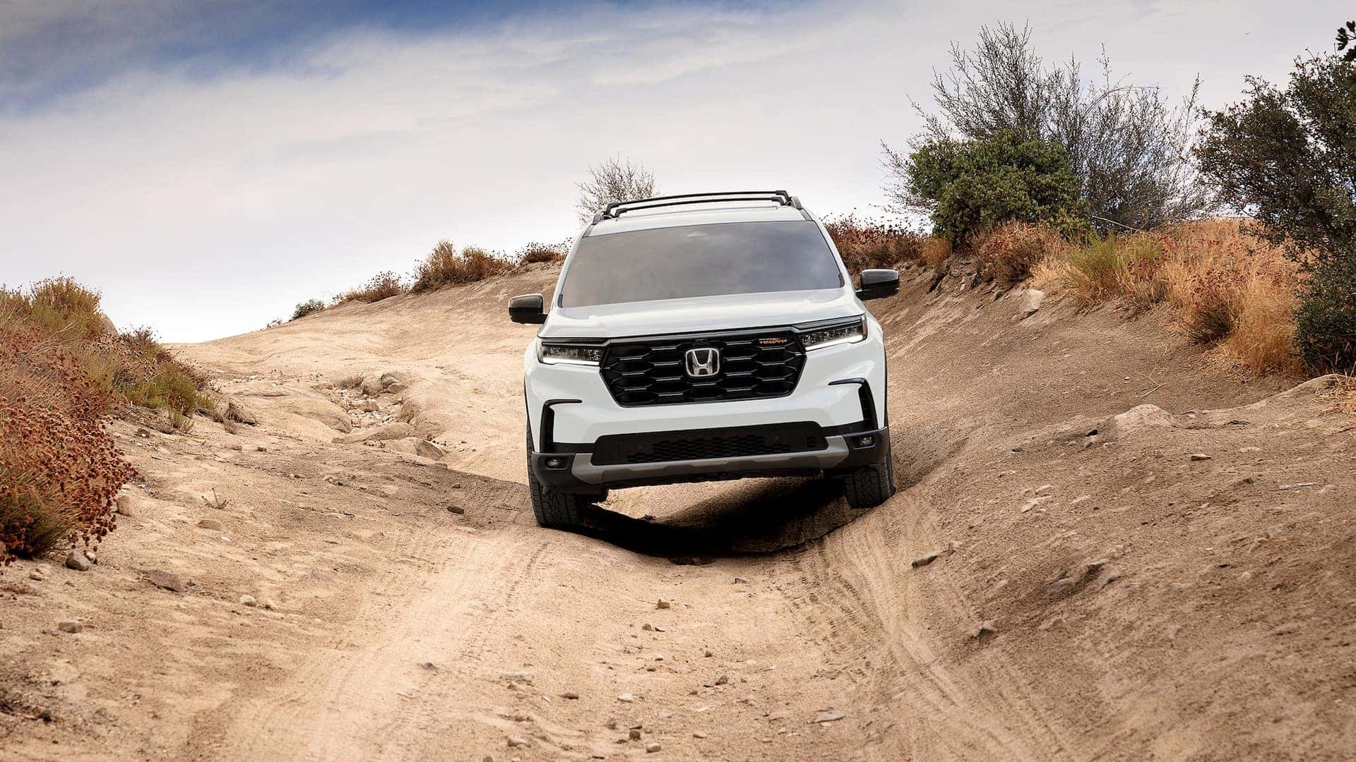 A front view of a white Honda Pilot driving downhill on a dirt road