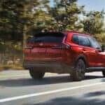 A red Honda CR-V driving down the road by a forest