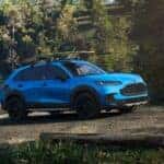 A blue Honda HR-V parked by a lake in a forest on a dirt road