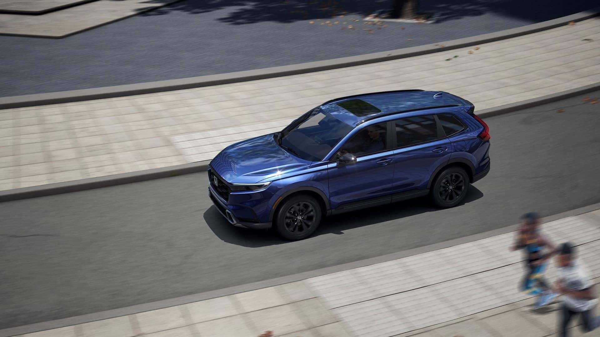 A blue Honda CR-V driving down the road by a pair of joggers