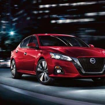 Front view of a red 2020 Nissan Altima driving through the city at night