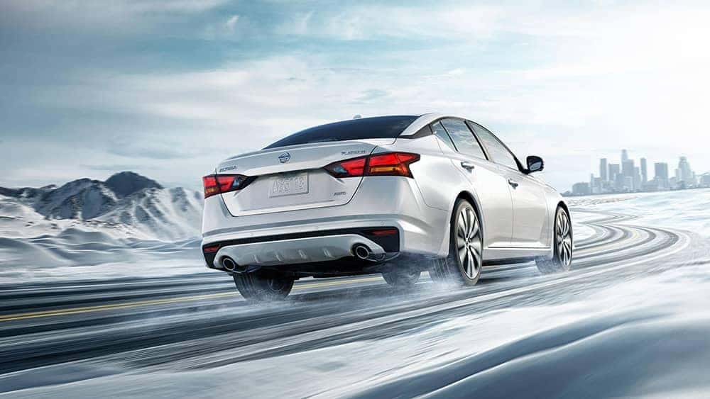 Rear view of a white 2020 Nissan Altima driving on a snowy road toward the city