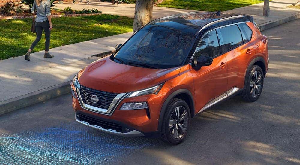 An orange 2022 Nissan Rogue Platinum is shown driving through the suburbs.