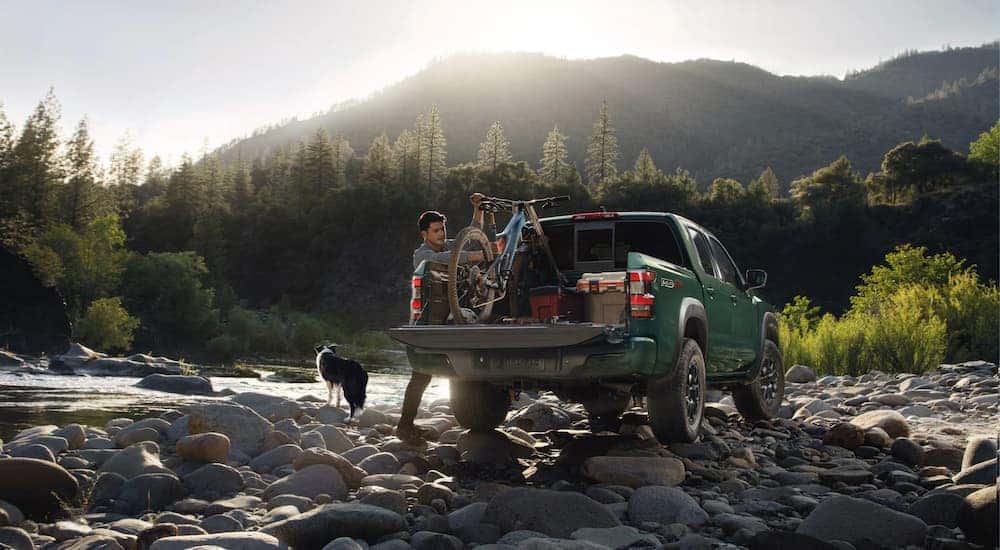 A man is shown taking gear out of bed of a green 2023 Nissan Frontier PRO-4X for sale.
