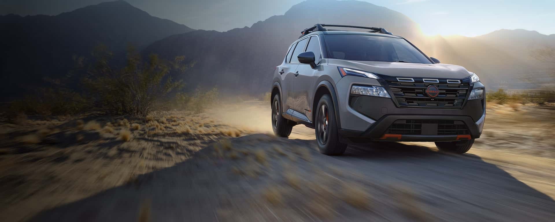 A gray Nissan Rogue driving through the desert on a dirt road