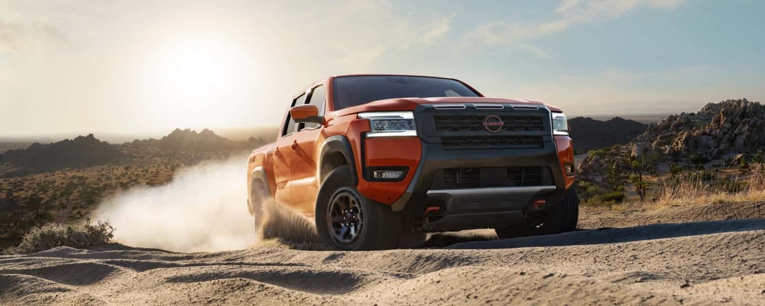 An orange Nissan Frontier driving over sand in a desert