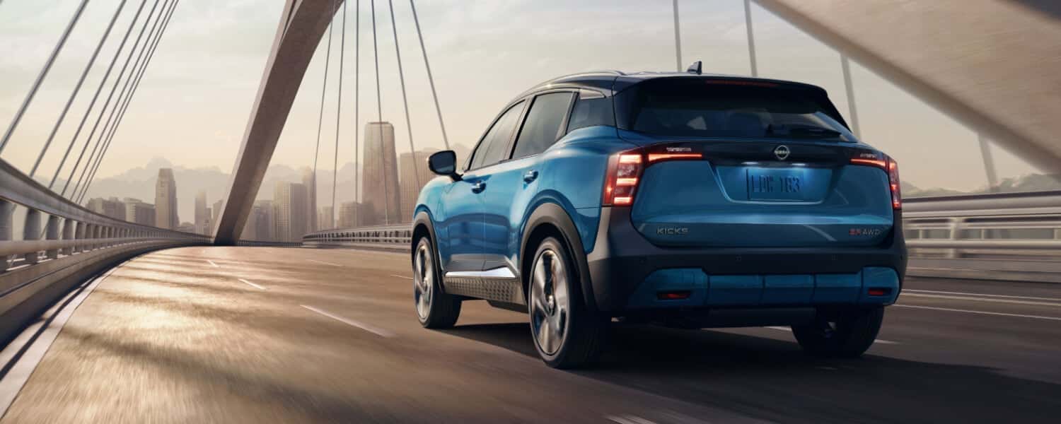 A rear view of a blue Nissan Kicks driving over a bridge towards a city