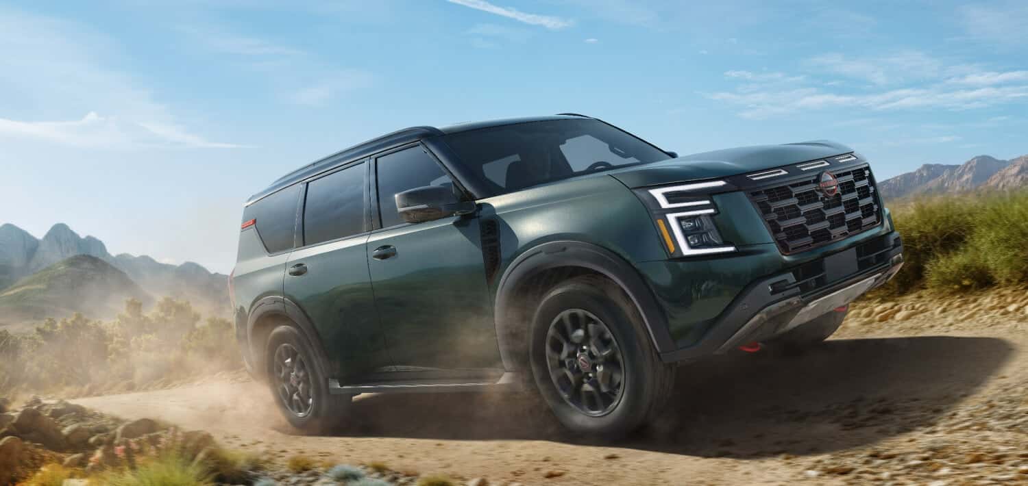 A green Nissan Armada driving over a dirt road and kicking up dust