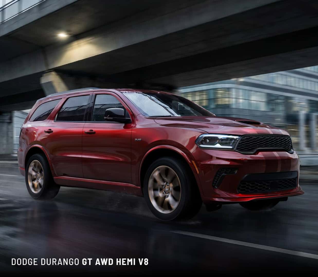 Front three-quarter view of a red 2027 Dodge Durango GT driving on a wet city road under an overpass.