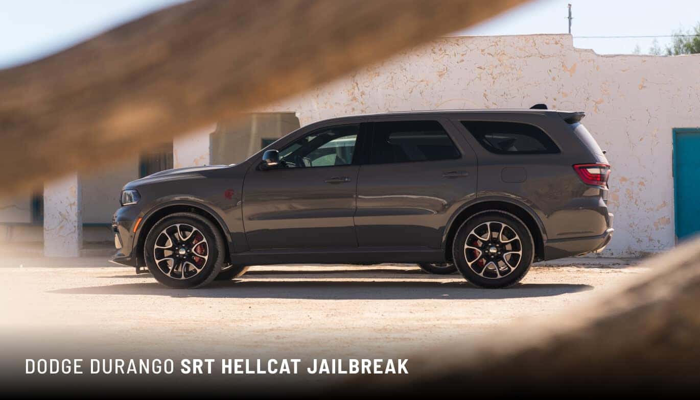 Side profile view of a dark grey 2027 Dodge Durango SRT Hellcat Jailbreak parked near a white building.