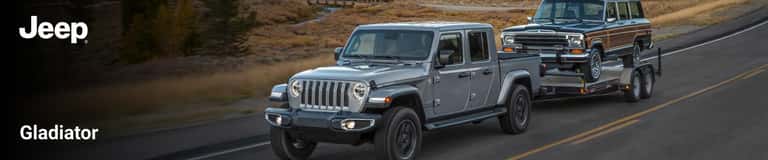 Front exterior view of silver Jeep Gladiator towing a station wagon down a country highway.