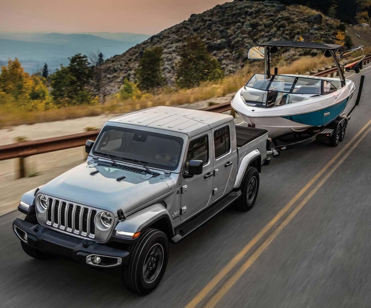 Close action shot of a silver Jeep Gladiator towing a boat on a mountain highway.