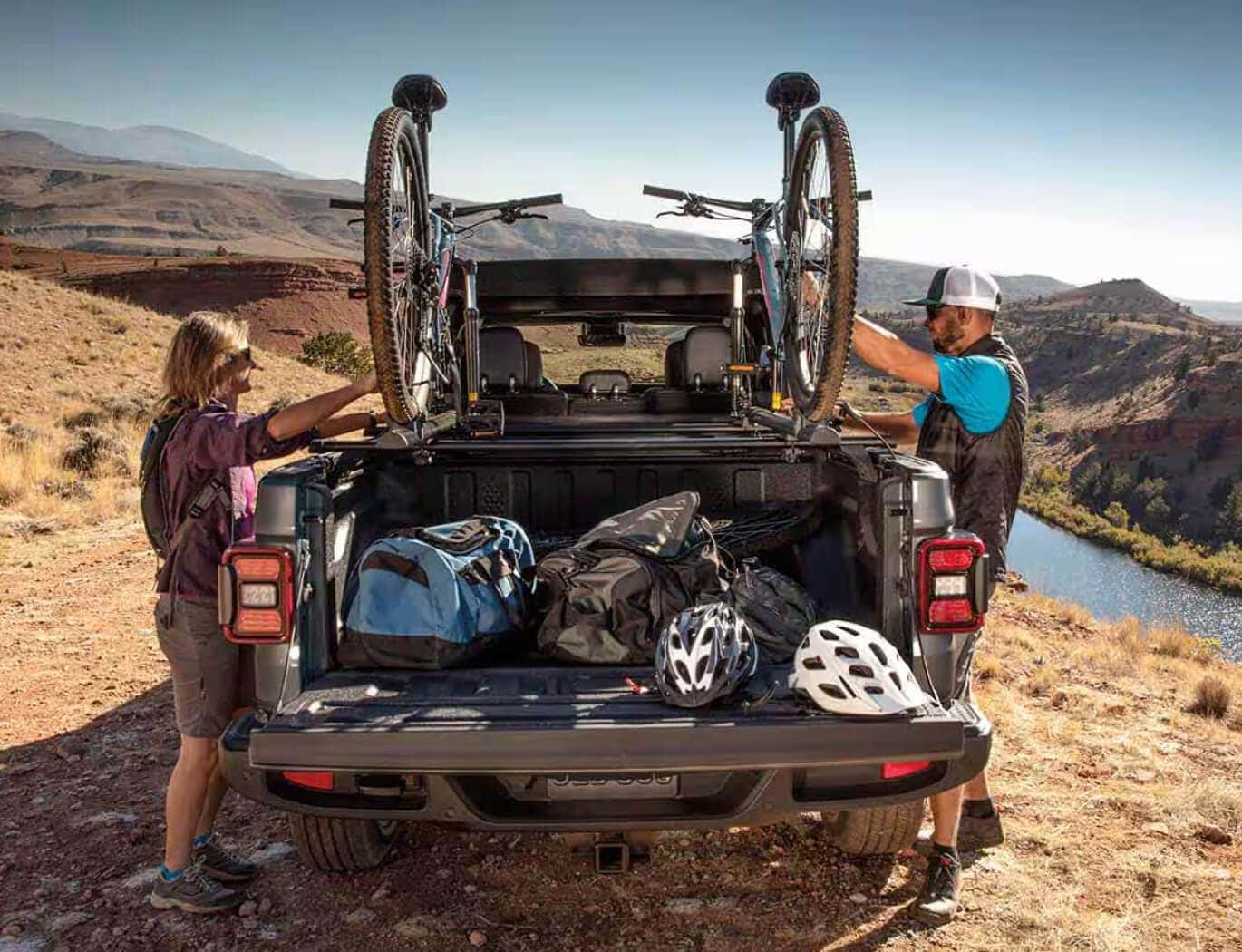 Close rear image of a couple unloading mountain bikes off a Jeep Gladiator bike rack.