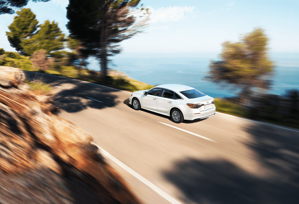 A white 2022 Civic Sedan driving along a beach or ocean road