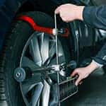 Mechanic adjusting a car's wheel alignment using a professional measuring tool in an auto repair shop. Close-up on the wheel and equipment.