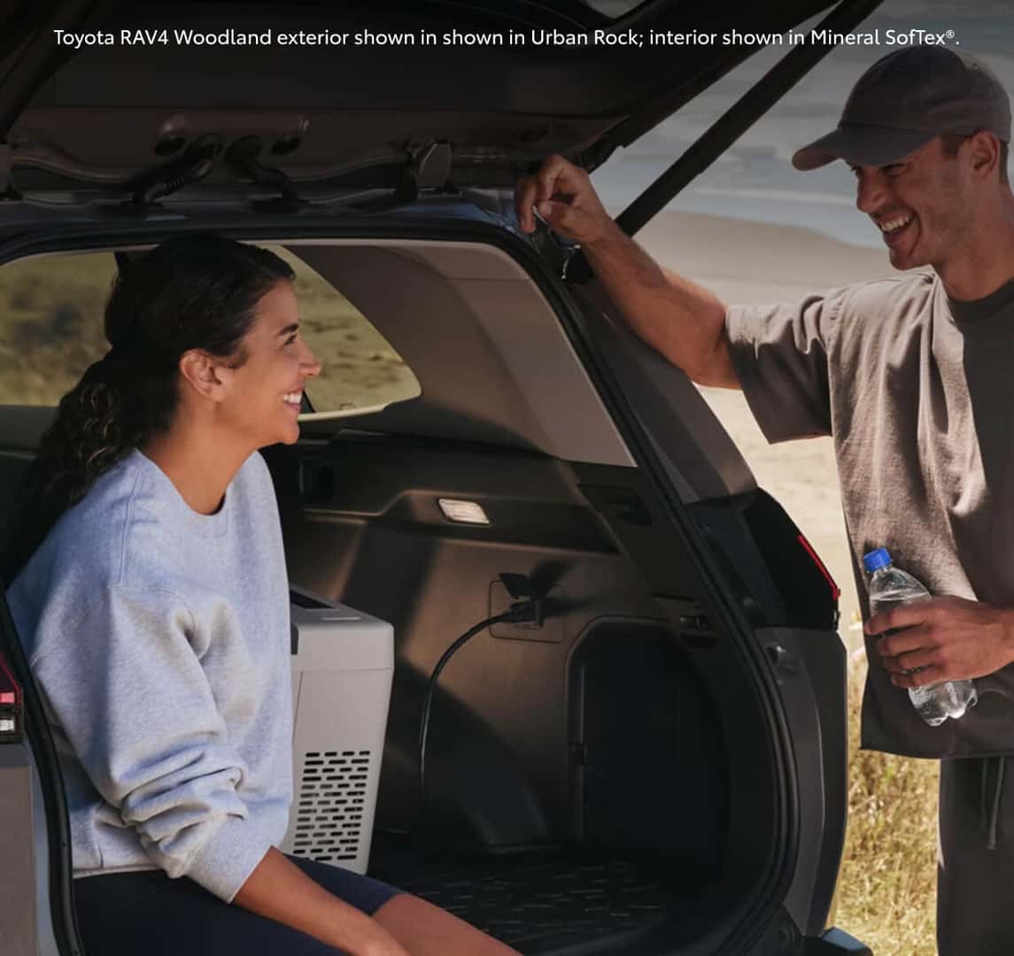 Rear cargo shot of a 2026 Toyota RAV4 Woodland Edition in Urban Rock, highlighting the 120V power outlet powering an electric cooler.