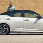 A person standing next to a white car with another person running towards it
