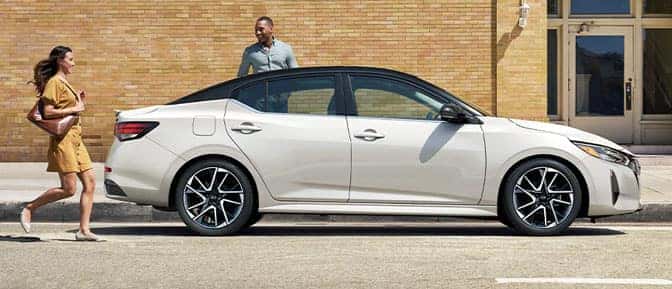 A person standing next to a white car with another person running towards it