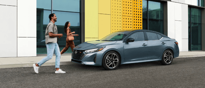 Two people walking by a gray car