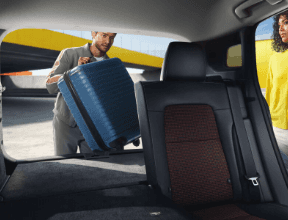 A person carrying a suitcase in the back of a car