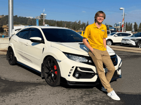 A man wearing a yellow shirt leaning against a used 2018 Honda Civic