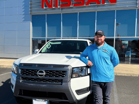 A man standing by a new white 2025 Nissan Frontier parked in front of a building