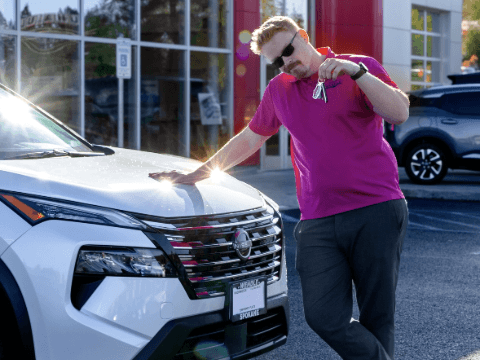 A man wearing a bright pink shirt holding keys leaning on a new 2025 Nissan Rogue