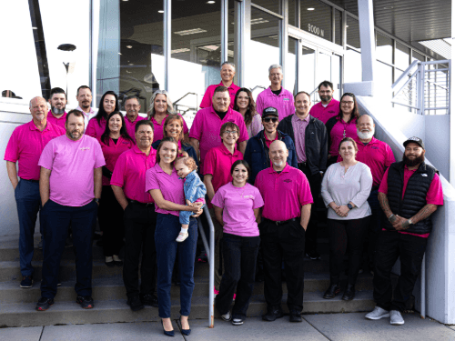 Group of Wendle dealership staff wearing pink shirts on stairs for Breast Cancer Awareness.