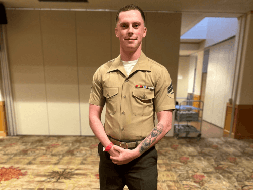 A man wearing a tan short-sleeve service uniform with his rank insignia and ribbon bar on the chest.
