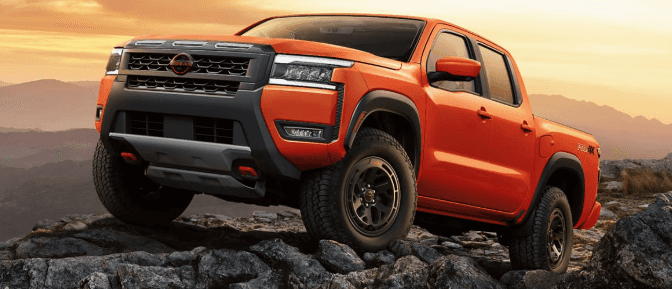 Nissan Frontier PRO-4X pickup truck in orange climbing over jagged rocks on an off-road trail at sunset.